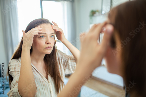 Woman examining forehead wrinkles in home mirror