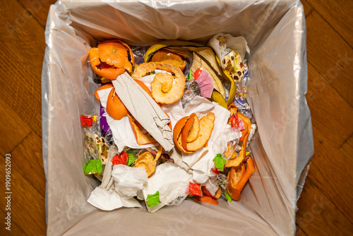 Trash bin filled with plastic packaging and household waste inside a kitchen. Overhead view photography. Household waste management and recycling concept.