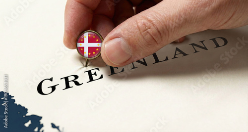 Hand pinning a pin with the Danish flag with yellow stars symbolizing the unity of Europe on a map of Greenland