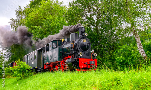 Photos A steam train with old locmotive on the Sauerland narrow-gauge railway rumbles along the narrow-gauge tracks through the summery Else Valley from Köbinghausen to Hüinghausen (Sauerland, Germany)