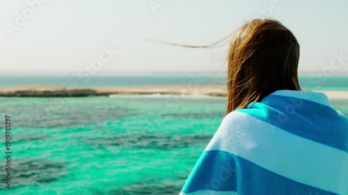 A woman stands on the upper deck of a yacht, wrapped in a towel, after swimming in the sea. She admires the crystal clear turquoise water. Sea travel, tourism.