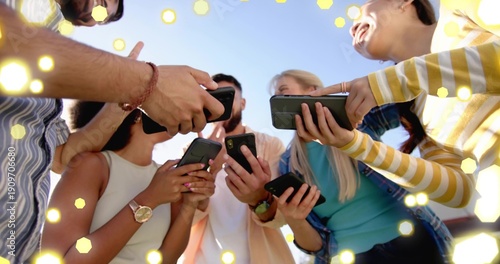 Holding smartphones, five friends leaning under blue sky, showing denim, watches and hex bokeh