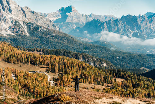 Tableau sur toile A man backpack stands overlooking autumn larch forest and Dolomites mountain in