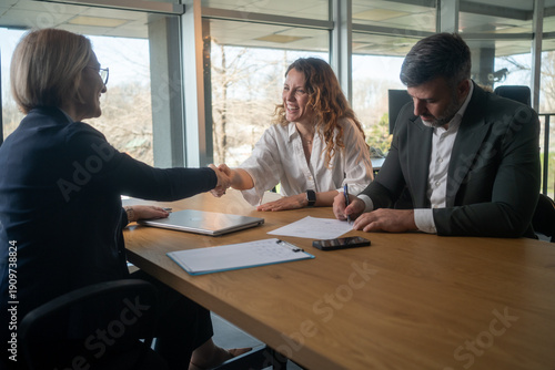 Financial advisor or bank worker shaking hands with young couple, successful deal