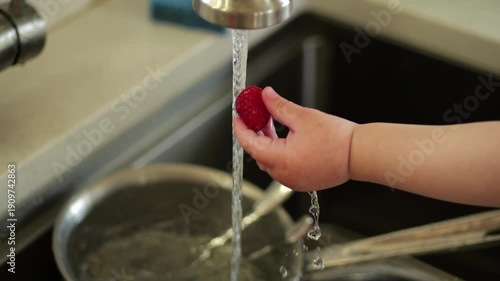 Child hand washing a fresh raspberry under tap water