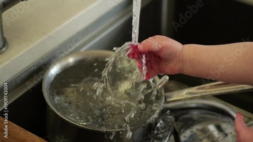 Child's hand washing raspberry in sink water