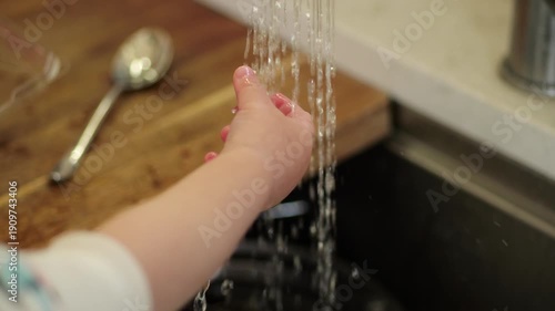 Curious baby hand playing with running tap water