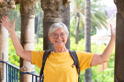 Happy Caucasian senior tourist woman in yellow jersey and glasses visiting the Real palace Alcazar in Seville, Spain - travel vacation concept