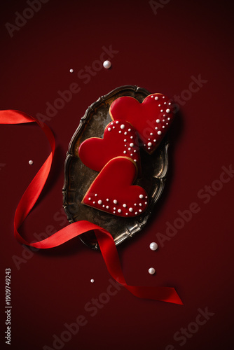 Valentine's Day. A gift of heart-shaped gingerbread cookies on a metal tray with a red ribbon on a red background.