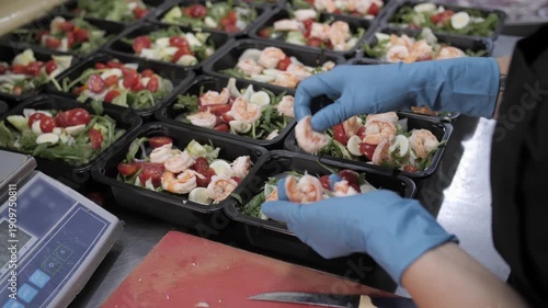 Gloved worker preparing shrimp salad meal trays for catering.