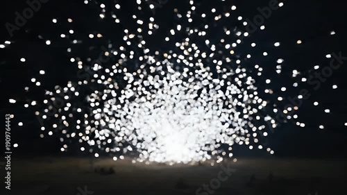 Blurred white lights sparkle against a dark, night sky above a dark field