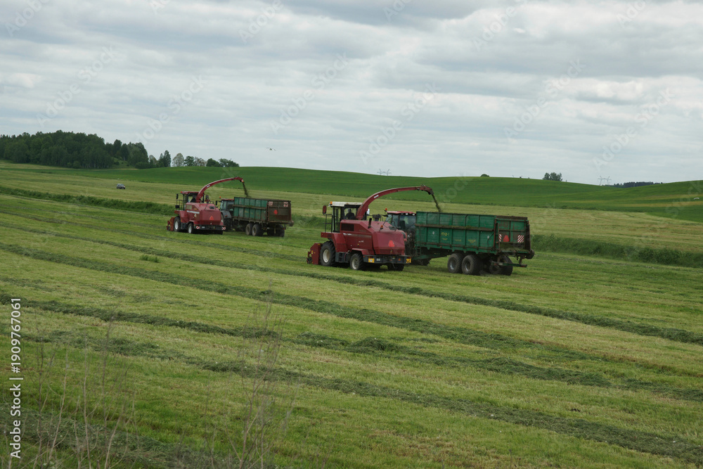 Obraz premium Machines work together to harvest grass in a field on a cloudy day near a rural area in summer