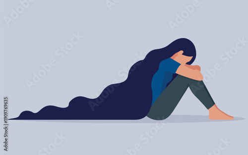 A solitary young woman with long dark hair sits on the floor appearing sad and withdrawn