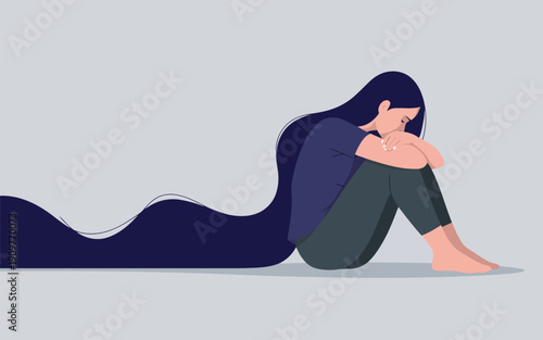 A thoughtful woman sits holding her knees on the floor with dark hair flowing behind her