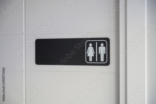 Black horizontal sign with white symbols of man and woman on a white toilet door