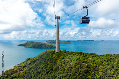 Foto Aerial view of a cable car traveling over green hills and turquoise waters, with distant islands visible under blue sky