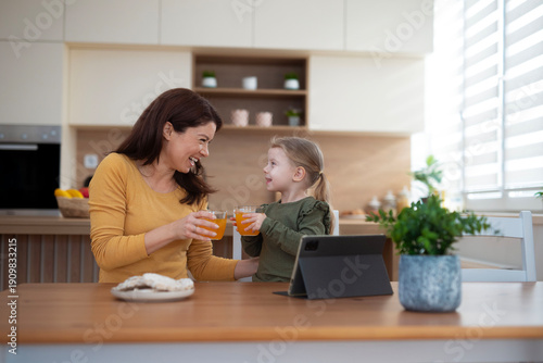 Mother and daughter drinking juice, bonding in kitchen