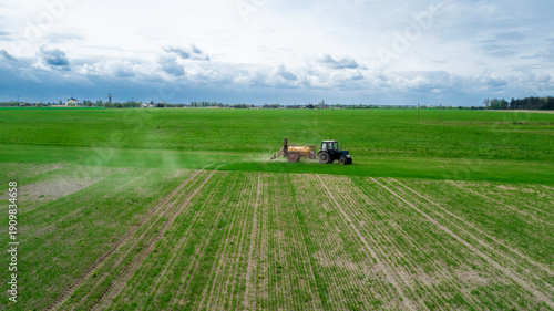 Obraz na plátne Aerial view, Farmer on a tractor with a sprayer makes fertilizer for young veget