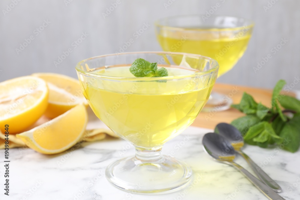 Fototapeta premium Yummy yellow jelly in dessert bowls, mint and fresh lemons on white marble table, closeup