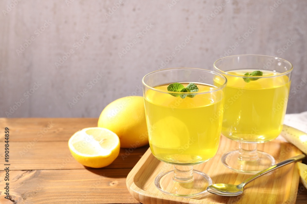Fototapeta premium Yummy yellow jelly in dessert bowls, mint and fresh lemons on wooden table, closeup. Space for text