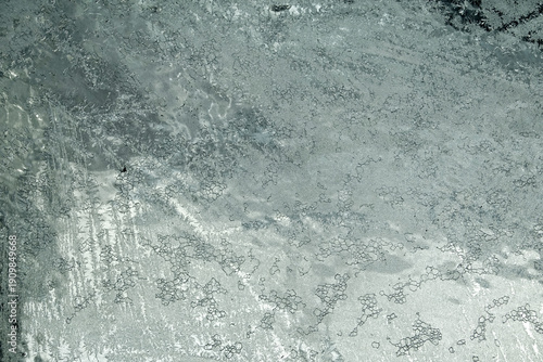 Close‑Up of Frost Patterns on an Icy Window in Winter. Close‑up of a window covered with intricate frost patterns and ice crystals formed during freezing winter temperatures. Icy abstract texture.