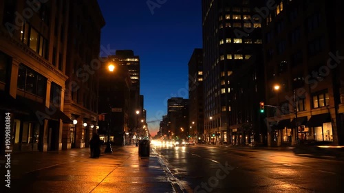 Static video of a busy city street at dusk with car headlights blurring into golden trails against dark skyscrapers under a deep blue sky. Concept of urban rhythm and evening life