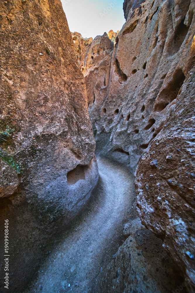 Obraz premium Narrow Slot Canyon Trail with Rugged Rock Walls and Natural Holes in Desert Landscape