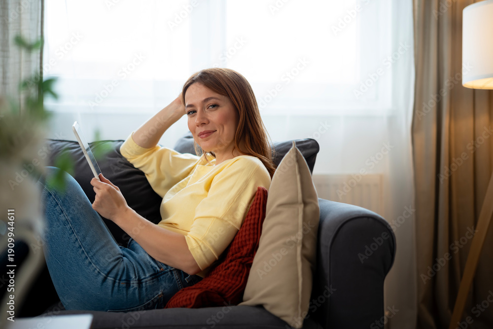Obraz premium Woman relaxing on sofa using digital tablet smiling