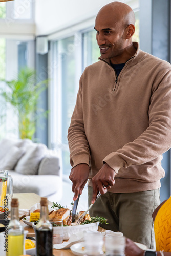 Indian friends gathering at open-plan dining area, man carving roast poultry and pouring juice