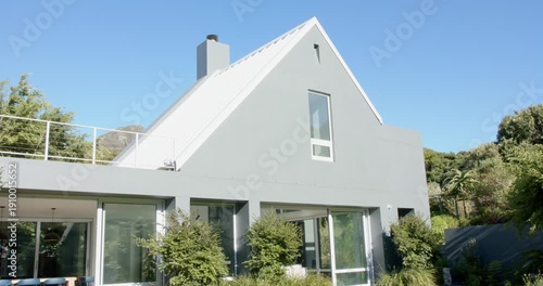 Camera is pulling back, showing two-story house with steep gable, balcony, glass doors, lawn