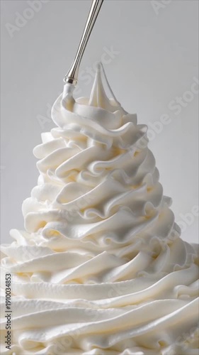 A spoon lifting a swirl of white whipped cream into a decorative pie shape on top of a dessert