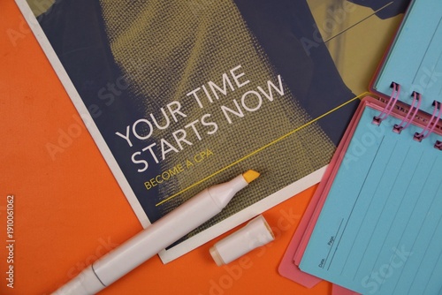 Quadro su tela orange surface features a motivational poster that reads 'Your Time Starts Now,' along with a yellow highlighter and a notebook