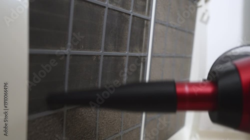 A close-up of a black and red vacuum cleaner attachment used to clean air conditioner filters shows the detailed cleaning inside the room.