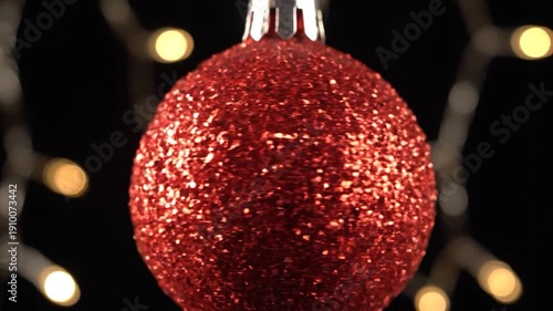 A sparkling red glitter ornament hangs against a festive bokeh background