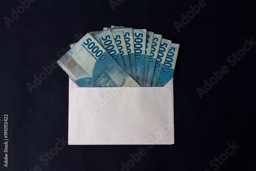 A fan of 50,000 IDR banknotes neatly tucked into a white envelope against a dark background, perfect for salary or holiday bonus concepts.