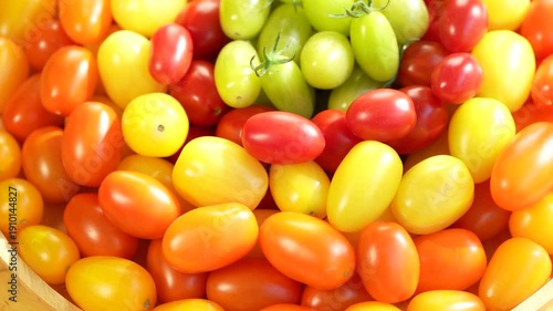 Colorful premium cherry tomatoes in red, yellow, orange and green tones filling the frame, fresh organic produce concept for healthy eating, vegan diet and farm to table food on wooden table.