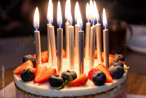 Festive birthday cake adorned with glowing candles, fresh strawberries, and blueberries. Perfect for joyful celebrations and special occasions