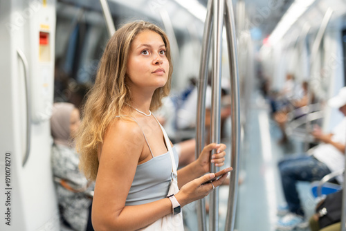 Thoughtful young girl standing in subway wagon holding mobile phone in hand