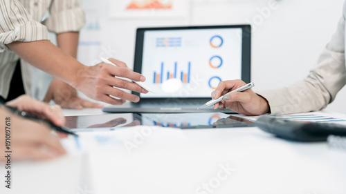 Business team discussing financial charts and data on a laptop during a meeting in a bright office.