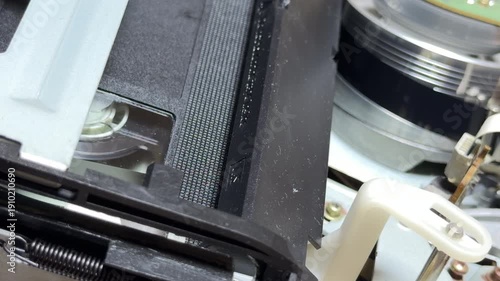A vintage VCR mechanism pulls a VHS tape into position for playback. The internal gears and rollers produce a rhythmic mechanical clatter and a soft, steady whirring sound.