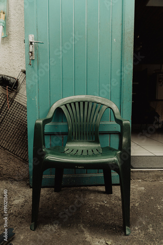 Chaise en plastique vert devant une porte turquoise dans un décor extérieur modeste