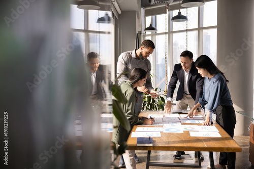 Tableau sur toile Four diverse business analysts discussing paper reports at meeting table, analyzing statistic research results, working together in business plan for project growth
