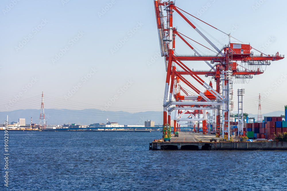 Fototapeta premium Industrial Gantry Cranes at Osaka Bay Harbor Port, Japan. Large container cranes at commercial shipping terminal in Osaka, highlighting global logistics, maritime trade, and industrial infrastructure.