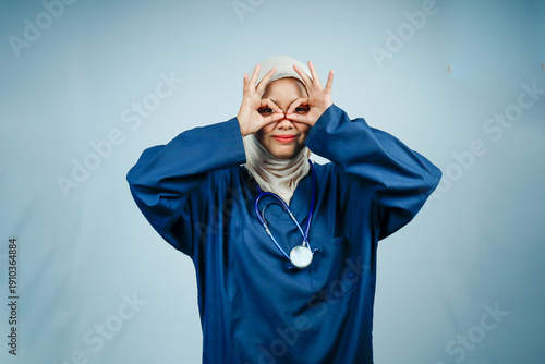 Playful Muslim female nurse in hijab and blue scrubs making 