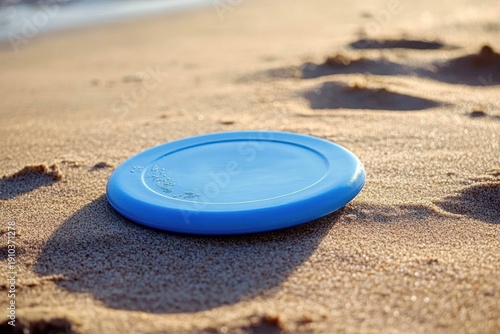 blue plastic flying disc resting on sunlit sandy beach with footprints and warm golden light, evoking relaxed playful summer leisure