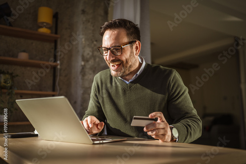 Fotografie Man enjoying safe online shopping with credit card on laptop
