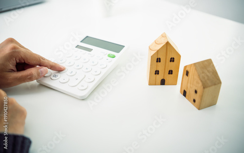 Photography Mortgage calculation concept with hand using calculator beside wooden house models planning home loan property investment and residential finance management