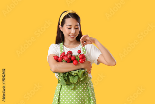 Young Asian housewife with ripe radish on yellow background