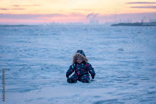 Child wandering the icy landscape as the industrial skyline fades into sunset colors