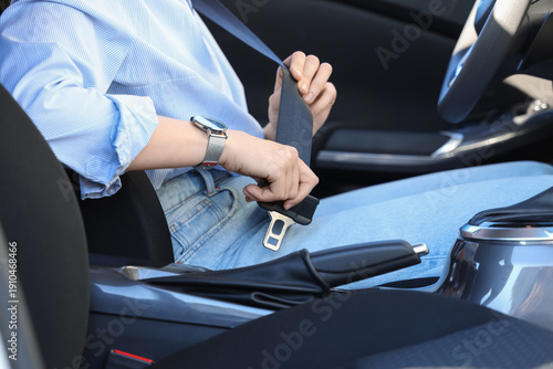 Fotografie Young woman fastening seat belt in car, closeup